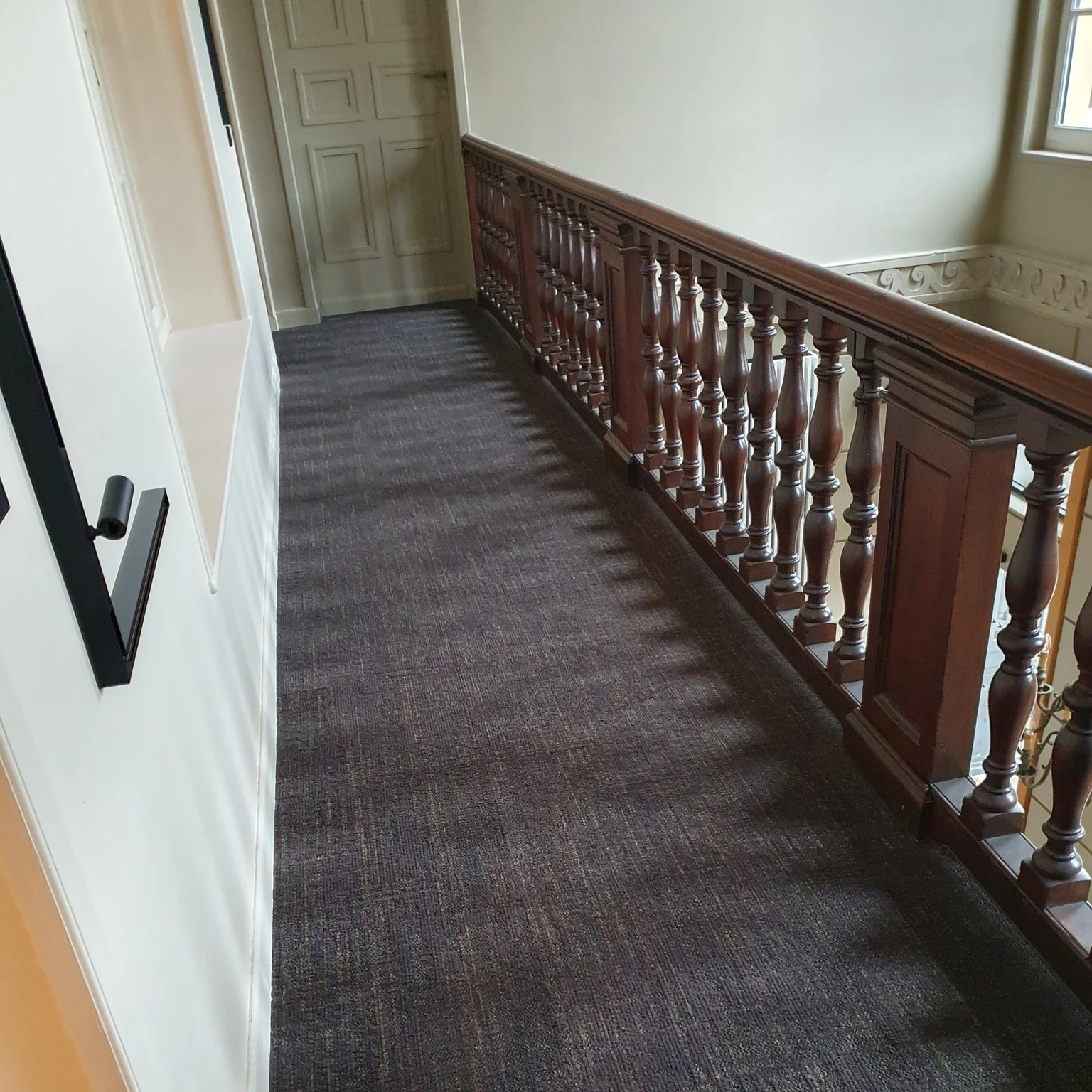 Intérieur minimaliste avec fauteuil beige à structure bois clair, table basse blanche cubique, étagère murale design en forme de branche d'arbre en bois foncé avec livres et plante