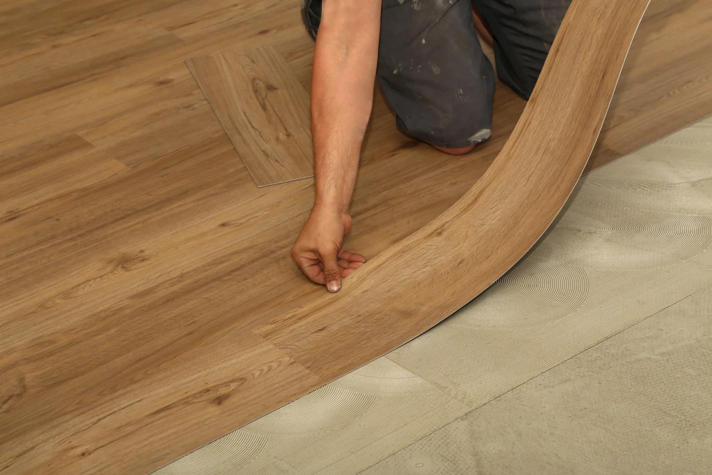 Intérieur résidentiel avec artisan à genoux installant un parquet contrecollé aspect chêne naturel sur sous-couche isolante