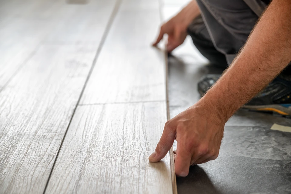 Artisan à genoux installant du parquet dans une pièce blanche, mesurant une lame avec un mètre ruban